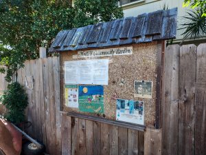This photo shows the bulletin board at the Mo'ili'ili Community Garden. The board has been attached to a fence running alongside the garden, and contains meeting info and the garden rules.